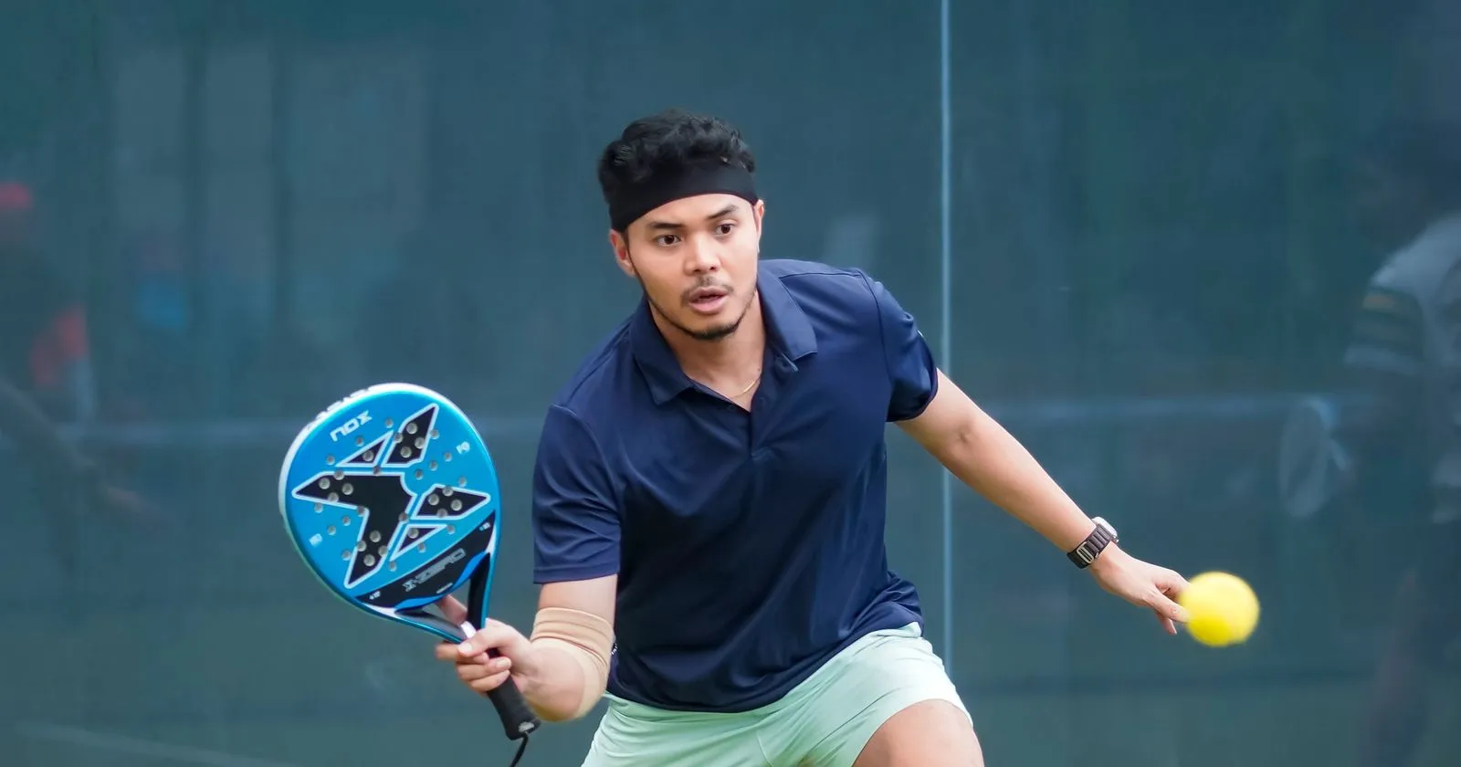 Joueur de padel portant une montre connectée, frappant la balle sur un court en gazon