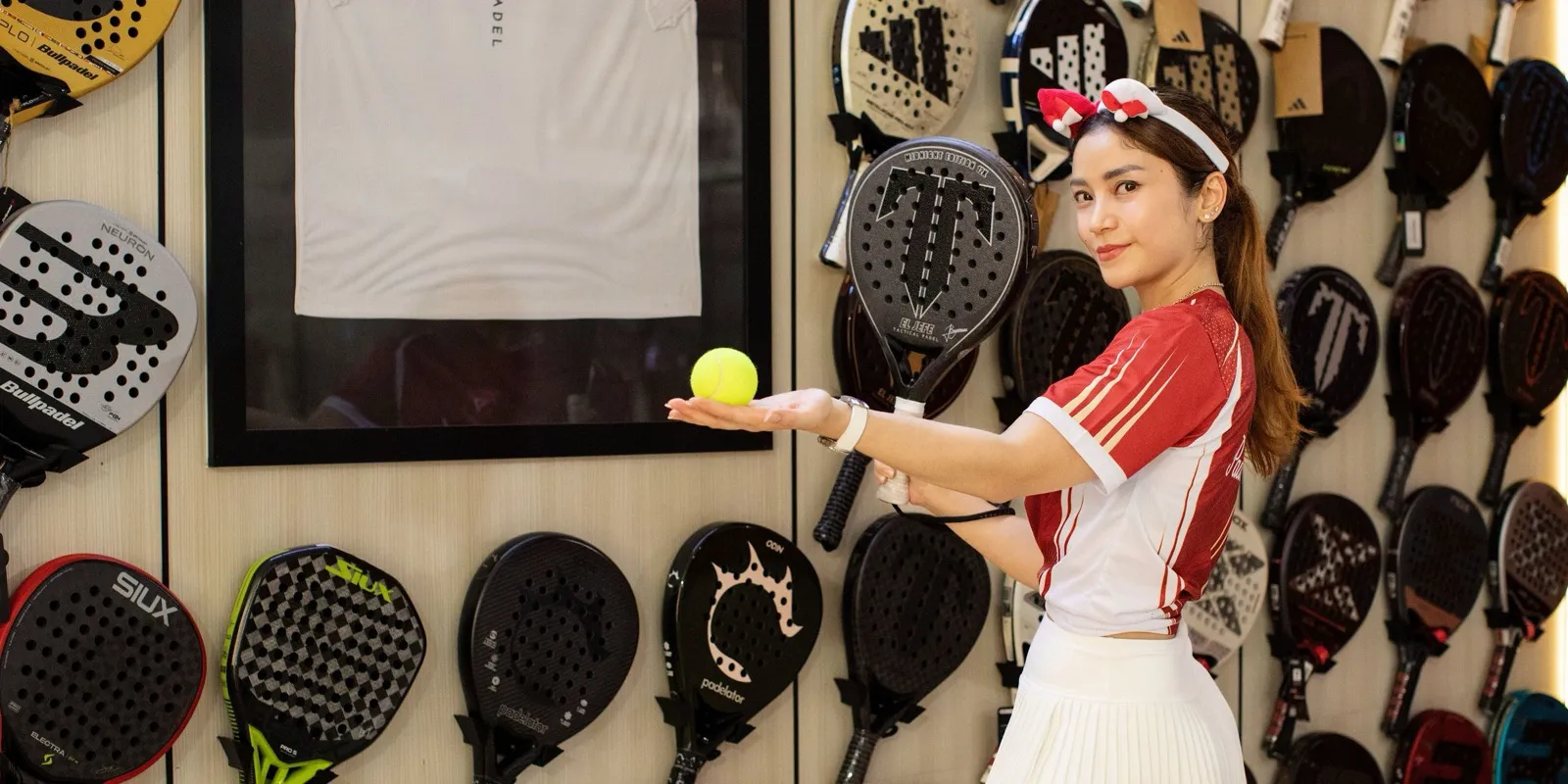 Jeune femme tenant une balle devant un mur de raquettes de padel en magasin