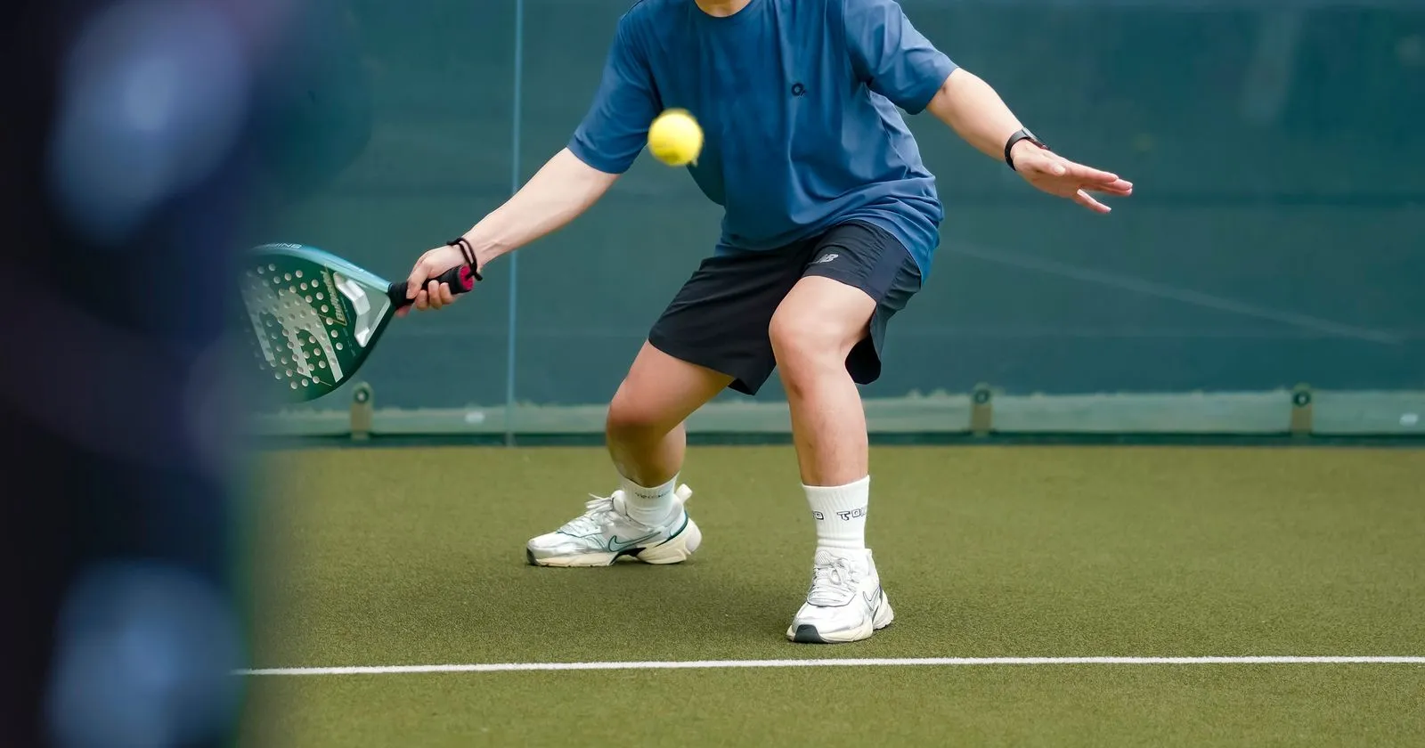 Joueur en appui fléchi sur le gazon synthétique d’un court de padel, en chaussures blanches