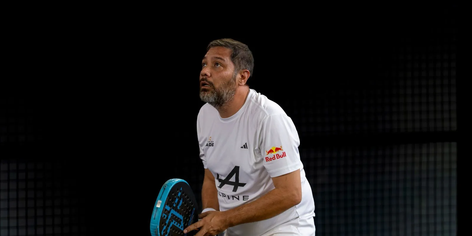 Joueur de padel concentré en position d’attente sur un court intérieur sombre
