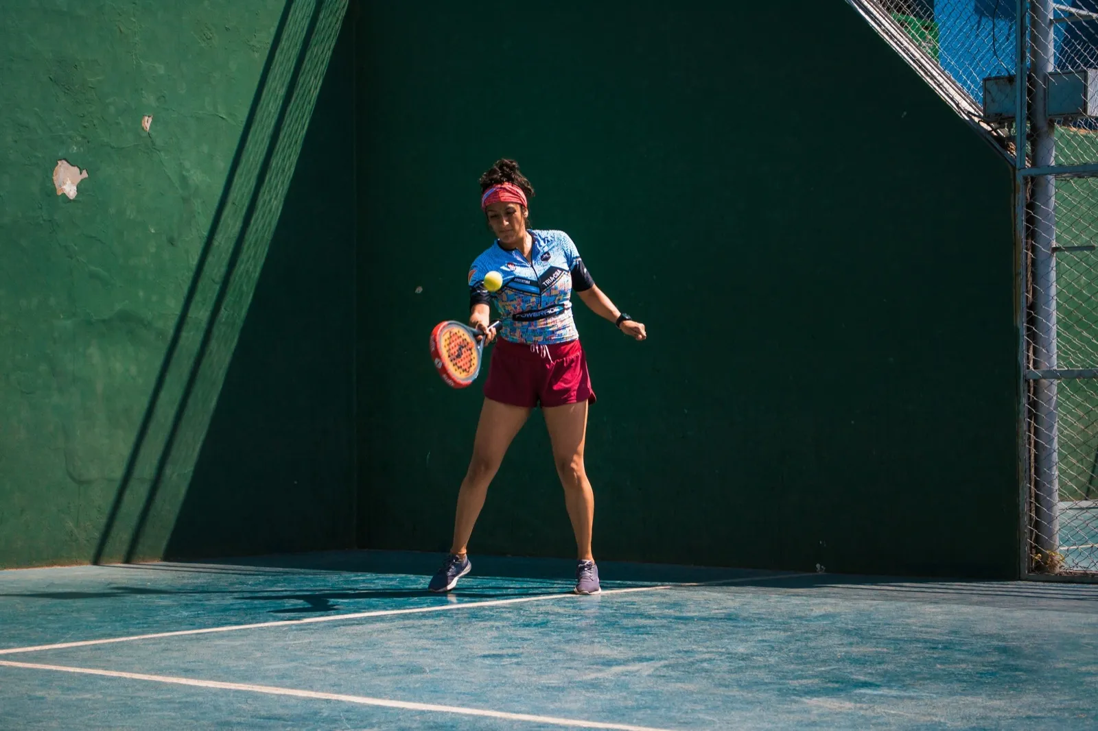 Joueuse de padel frappant un coup droit sur un court bordé de murs verts