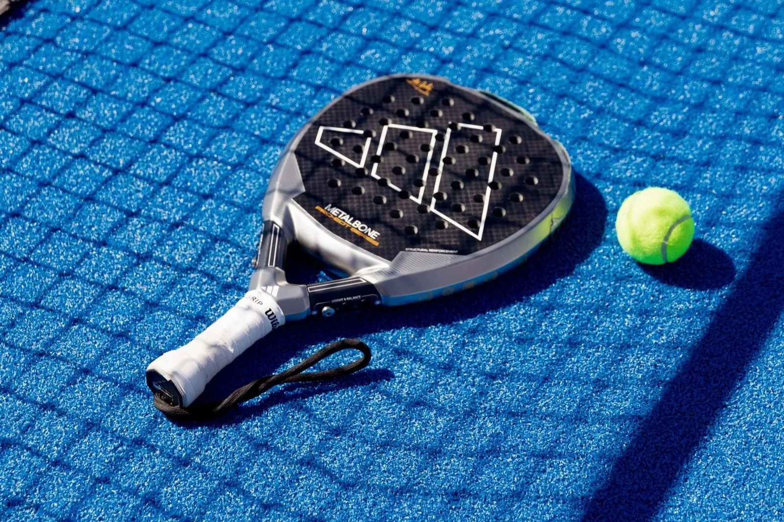 Raquette de padel et balle jaune posées sur un court bleu près du filet